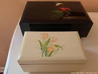 Two lacquerware music boxes, one black with floral bird, one white with tulips.