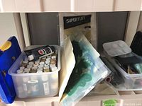 Wide-angle photo showing plastic bin with paint bottles, folder containing wall stencils, and clear box with painting supplies