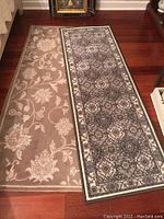 Two foam backed rug runners displayed side by side on wood floor, one beige with floral patterns, one gray with detailed geometric and floral patterns
