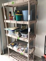 Full view of Rubbermaid beige four-tier plastic storage shelf loaded with various household items to demonstrate size and condition. Needs cleaning and contents not included.