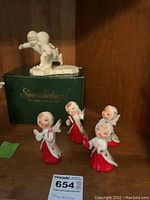Snowbabies porcelain figurines including pair of ice skaters and four angels on display shelf with original green box labeled 'Snowbabies'.
