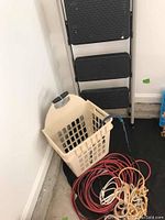 Photo showing beige plastic basket and coiled red and white cords on the floor against a white wall