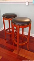 Two wooden spinning stools with black vinyl seats and studded perimeter, standing on hardwood floor.