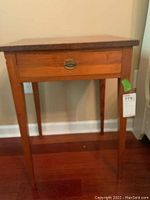 Front view of solid wood side table with one drawer and brass pull.