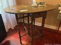 Full view of solid wood gate leg table with drop leaf sides and single drawer on turned legs.
