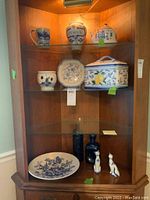 Wide view of china cabinet containing blue and white ceramics, plates, urns, decorative bottles and cat figurines