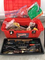 Wide shot of red Home Depot plastic toolbox filled with various tools and hardware items including glue, screws, and hand tools.