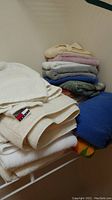 Stack of various folded towels including white towels with Tommy Hilfiger tags and others in grey, pink, blue, and cream.