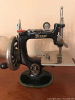 Front and side view of vintage small Singer toy sewing machine showing black enameled body and hand crank.