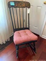 Front view of the vintage black wooden rocker with fruit motif painted on top backrest and red gingham cushion on seat.