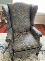 Front view of wing back chair showing detailed blue patterned upholstery, cushioned seat and backrest, curved arms and dark wooden legs.