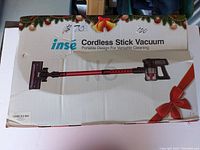 Photo of the INSE cordless stick vacuum box with a festive design and image of vacuum.