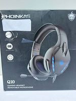 Front view of PHOINIKAS Q10 gaming headset box showing headset image and key features like USB plug, removable microphone, and battery info.