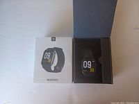 Smart Watch WATCH1 with black band in original white packaging box.