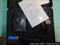 Open black plastic carrying case showing TENS 3000 device, 9V battery, wires, electrode pads, and manual.