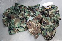 Overview of multiple woodland camouflage clothing items laid out including shirts and pants in size Large.
