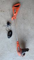 Complete cordless weed wacker laid out on concrete floor with charger and battery for size and completeness reference.