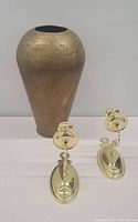 Single image showing one hammered brass vase and two brass sconces placed beside it.