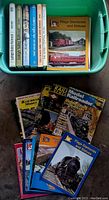 Photo showing assorted model railroad magazines and additional books laid out next to the green container holding the seven books.