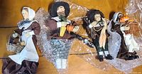 Four paper mache pilgrim figurines dressed in traditional attire, displayed on a wooden surface with bubble wrap protecting some parts.