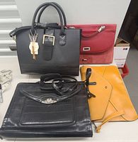 Four bags displayed including a black handbag with keychain, red portfolio bag, black clutch, and yellow clutch.