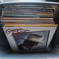 Side view of a box filled with vinyl LP records, front album is George Strait's 'Does Fort Worth Ever Cross Your Mind'. Other albums stacked behind are mostly country music records.
