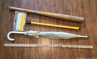 Top down view of vintage yardstick, wooden baseball bat, cleaning brush, and umbrella arranged parallel on wooden floor.