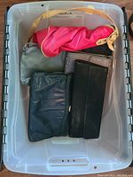 Plastic tote with five vintage purses and bags: pink bag with strap, silver small purse, light purple textured purse, large black clutch, and black wallet.