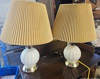 Pair of vintage table lamps showing full view with beige pleated shades and white ribbed orb bases on brass-tone metal stands.