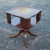Full view of the vintage wooden accent table showing square top, lower shelf, and curved legs with brass lion paw feet.