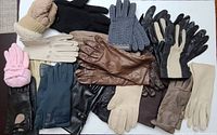 Top-down view of 13 pairs of women's gloves laid out on a flat surface, showing a variety of styles, colors, and materials.
