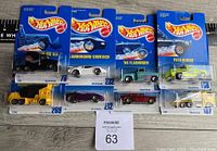 Full lot overview showing 8 Hot Wheels diecast cars in original Mattel blister packaging arranged in two rows on a wooden floor with a ruler for size reference.