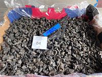 Close-up of black shredded rubber mulch pieces in a large plastic bin with measurement and auction tag showing approximate 15x20 coverage.