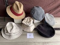 Full view of the six hats arranged on wooden surface with ruler showing size, including tan fedora with red band, two flat caps, two cream hats, and a black beret.