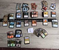 Multiple Magic the Gathering cards sorted in groups by color and type, showing a variety of card faces, including creatures, artifacts, lands, and tokens.