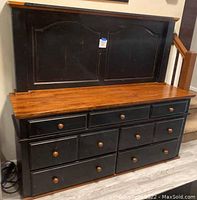 Solid wood dresser with seven drawers and an attached headboard with a top shelf, black paint with natural wood top surfaces.