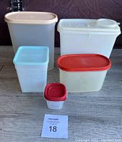 Various translucent and opaque plastic food storage containers with multiple colored lids in a group set on wooden surface