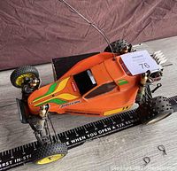 Top front side angle of vintage Kyosho Ultima 2WD off-road buggy in orange with green/yellow decals, Bridgestone branding, and antenna.