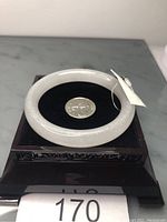 Translucent white jade bangle displayed on a decorative black stand with a tag visible, photographed from above with a quarter for size reference.