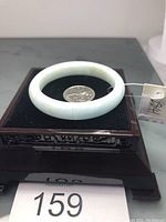 Front view of light blue aquamarine bangle bracelet displayed on a black padded stand with a quarter coin inside for scale.