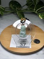 Front view of the Burma jade Buddha pendant displayed in a clear round holder with a coin for scale, placed on a wooden base.