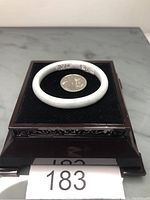 Top view of the small Burma jade bangle bracelet lying on black velvet cushion beside a quarter for size reference.