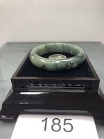 Front and top view of the natural Burma jade bangle on a black velvet cushion atop a wooden stand.