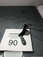 The green jade bean-shaped pendant on a black adjustable rope, showing overall appearance and size comparison with a quarter coin.