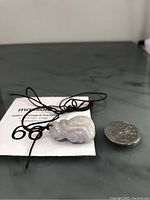 Burma jade money bag pendant with black cord completing the necklace, shown next to a coin for scale.
