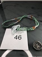 Full view of necklace laid out with the light green Burma jade money pendant and multi-colored jade bead rope.