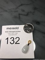 Photo showing the jade pendant alongside a coin for size reference on a MaxSold auction card.