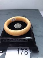 Yellow jade bangle displayed on a black velvet cushion with a coin for size comparison and a label sticker showing size 51-19.