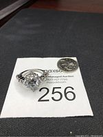 Front view of the silver tone ring with a large round central crystal and smaller accent crystals on the band, displayed next to a quarter for size comparison.