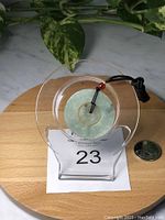 Front view of the double round jade pendant displayed on a clear stand with a quarter for size reference.